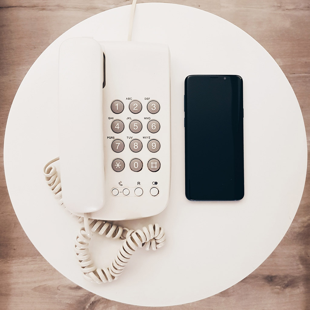 A telephone and mobile phone sitting side by side on a white plate.
