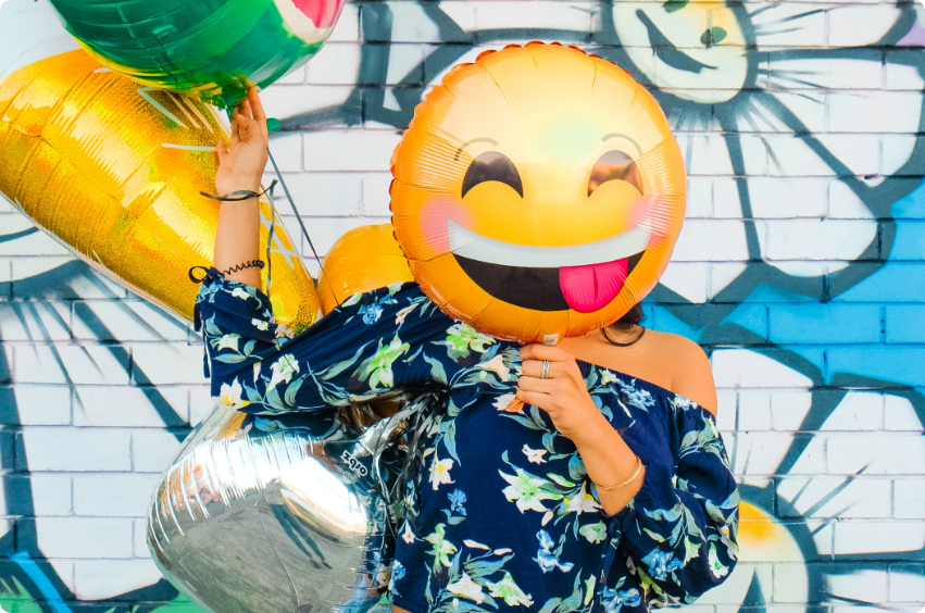 A creative shot of a woman with a smile-painted balloon masking her face
